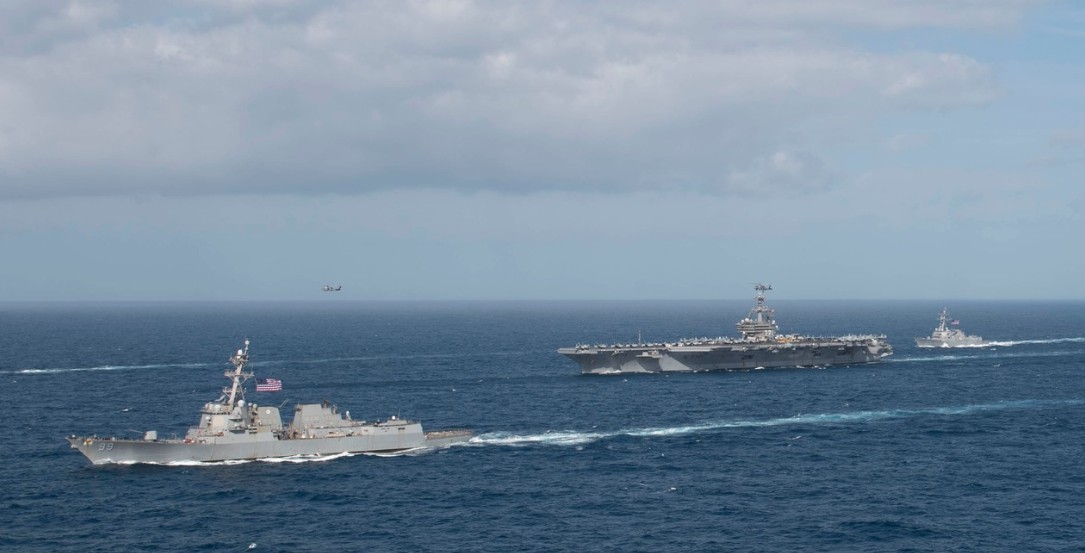 A tactical satellite graphic showing three US aircraft carriers positioned in the Persian Gulf and Arabian Sea, overlaid with red warning icons representing covert sabotage and intelligence alerts.