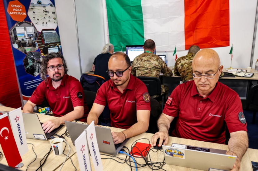 Military personnel from various allied nations operating advanced command and control software interfaces in a joint command center during a NATO exercise.