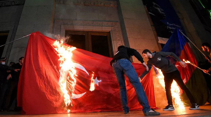 A geopolitical conceptual image showing the flags of Turkey and Azerbaijan, juxtaposed against a blurred background of protesters in Yerevan's Republic Square, with a diplomatic chess piece in the foreground.
